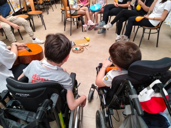 Bambini in carrozzina in un cerchio di musica, con una chitarra e strumenti a percussione