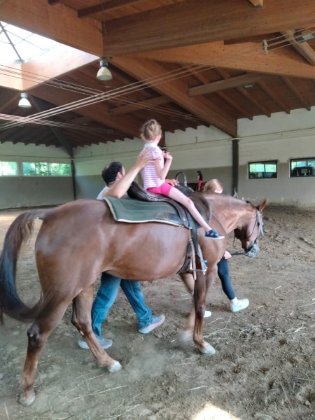 Una bambina a cavallo nel maneggio, accompagnata a piedi da due adulti
