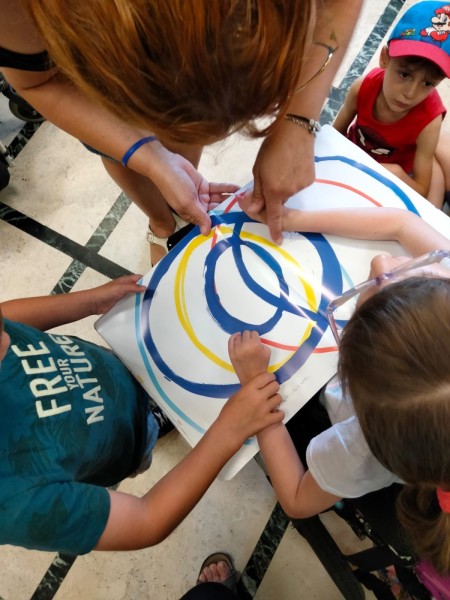 Bambini e un'educatrice dipingono insieme cerchi colorati su un foglio