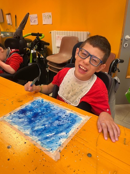 Un bambino sorridente al tavolo, accanto al suo dipinto blu