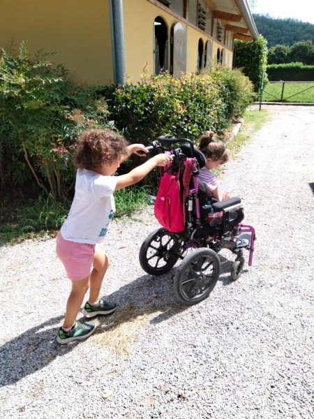 Una bambina spinge la carrozzina di un'amica su un vialetto all'aperto