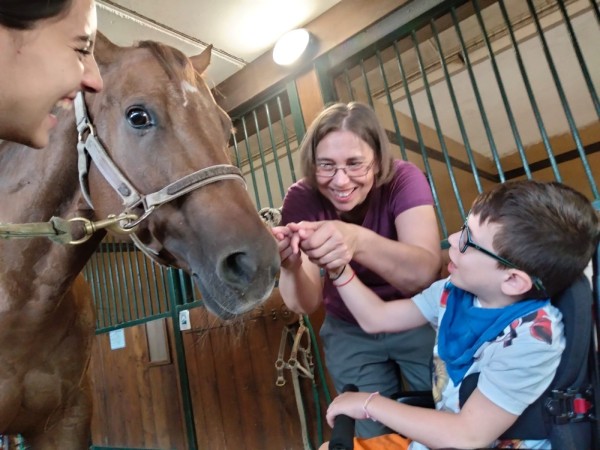 Un bambino in carrozzina accarezza un cavallo insieme a due educatrici