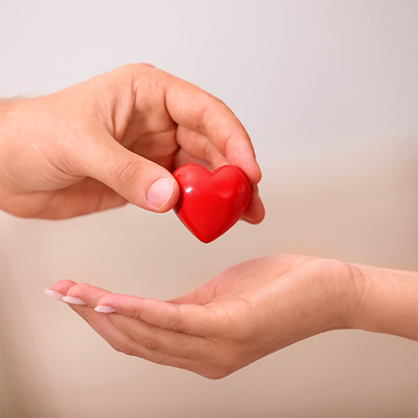 Una mano porge un cuore rosso a un'altra mano aperta